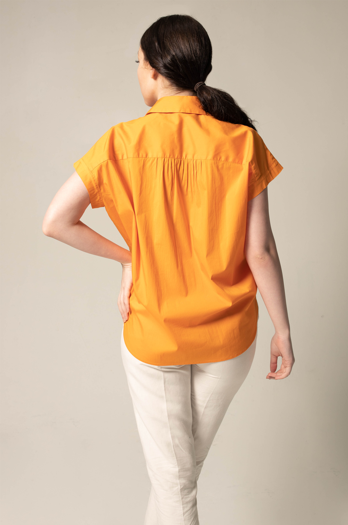 Person wearing an orange shirt and white pants against a plain background