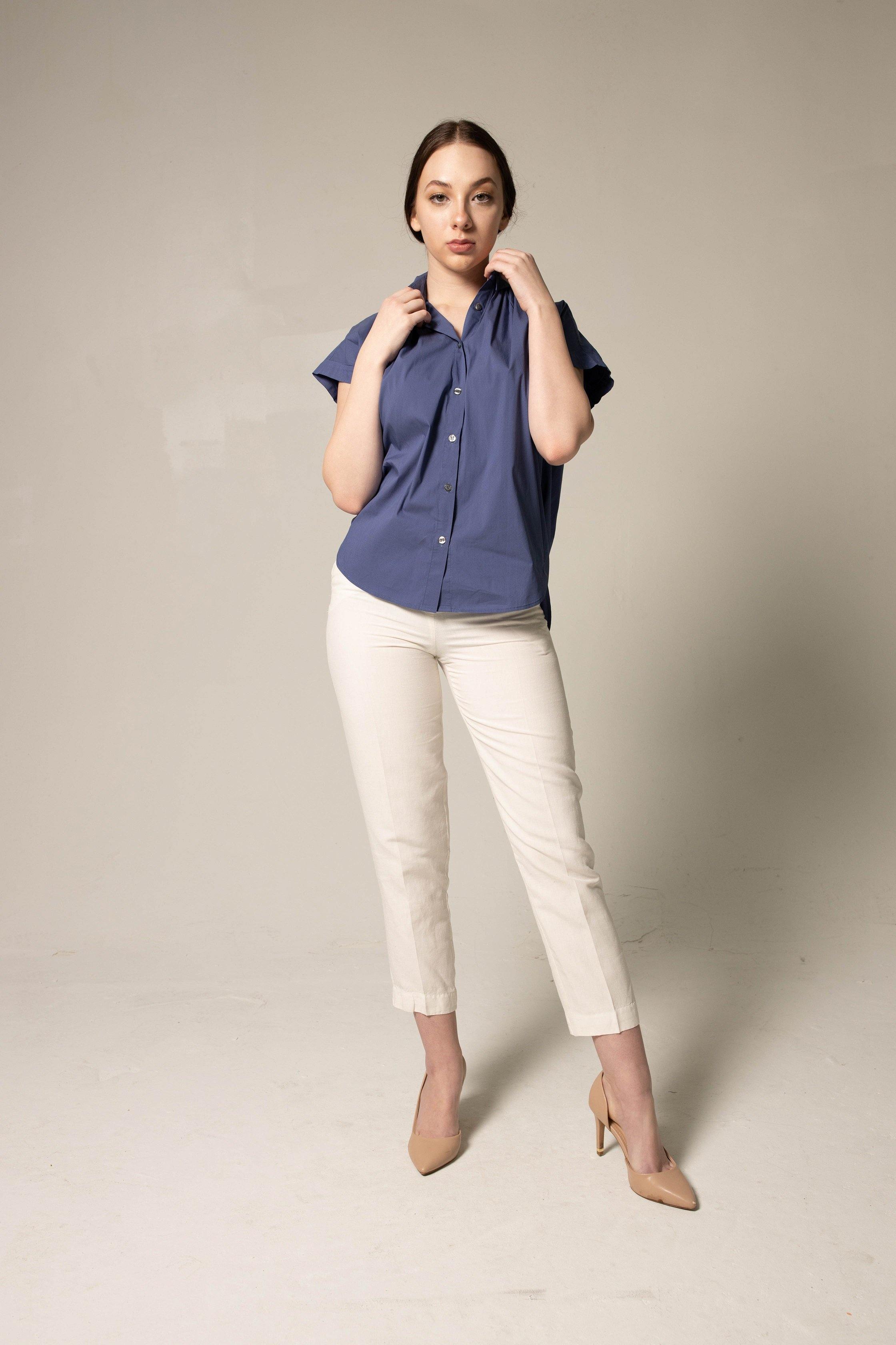 Woman wearing a blue shirt and white pants against a plain background