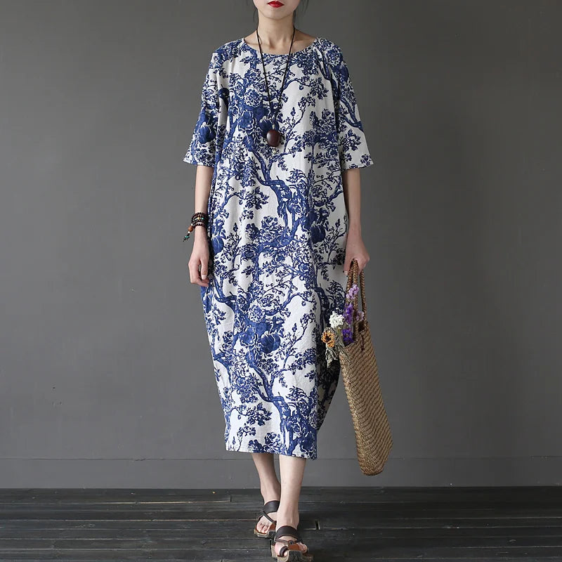 Woman wearing a blue and white floral dress holding a straw bag against a gray background