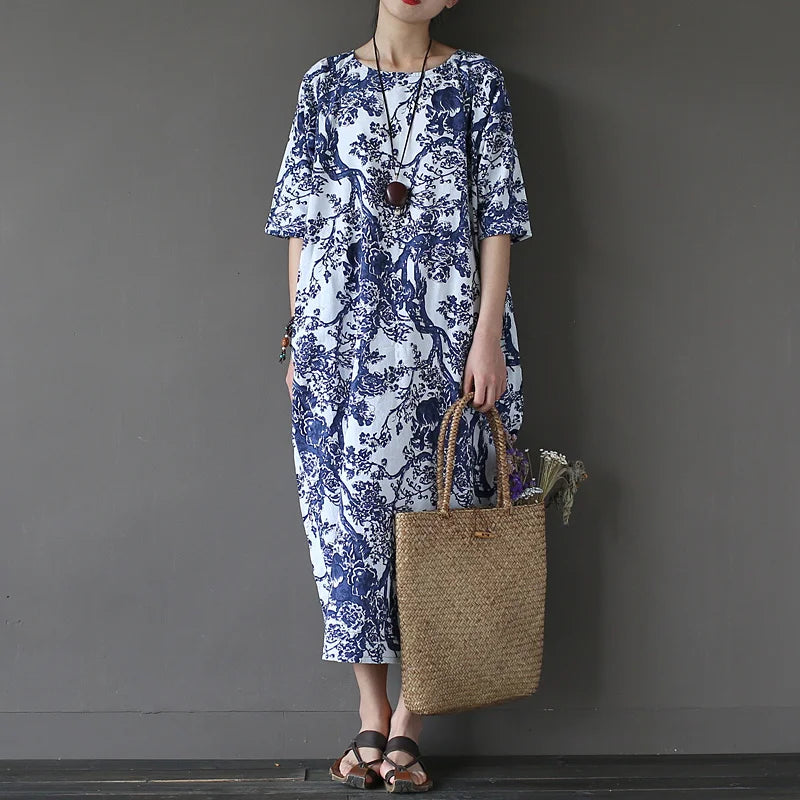 Person wearing a blue and white floral dress holding a woven bag against a gray background