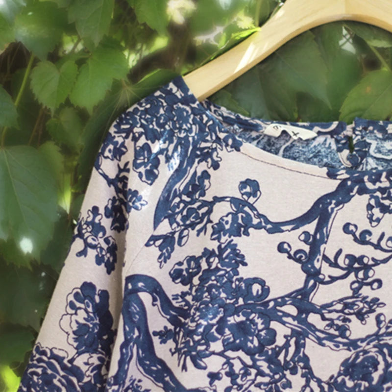 Blue and white floral patterned fabric on a wooden hanger against a green leafy background