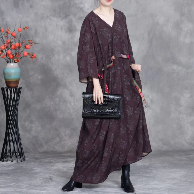 Person wearing a dark patterned dress holding a black handbag against a gray background