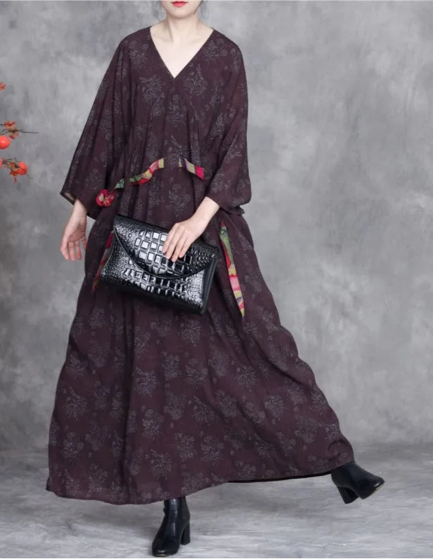 Woman wearing a long dark dress holding a black handbag against a gray background
