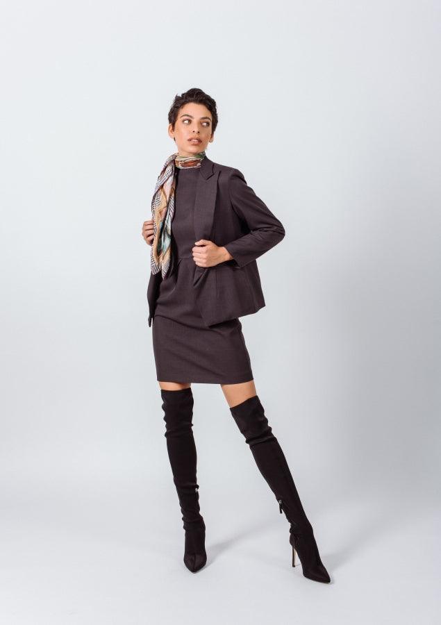 Woman wearing a brown suit with a scarf and black knee-high boots on a white background