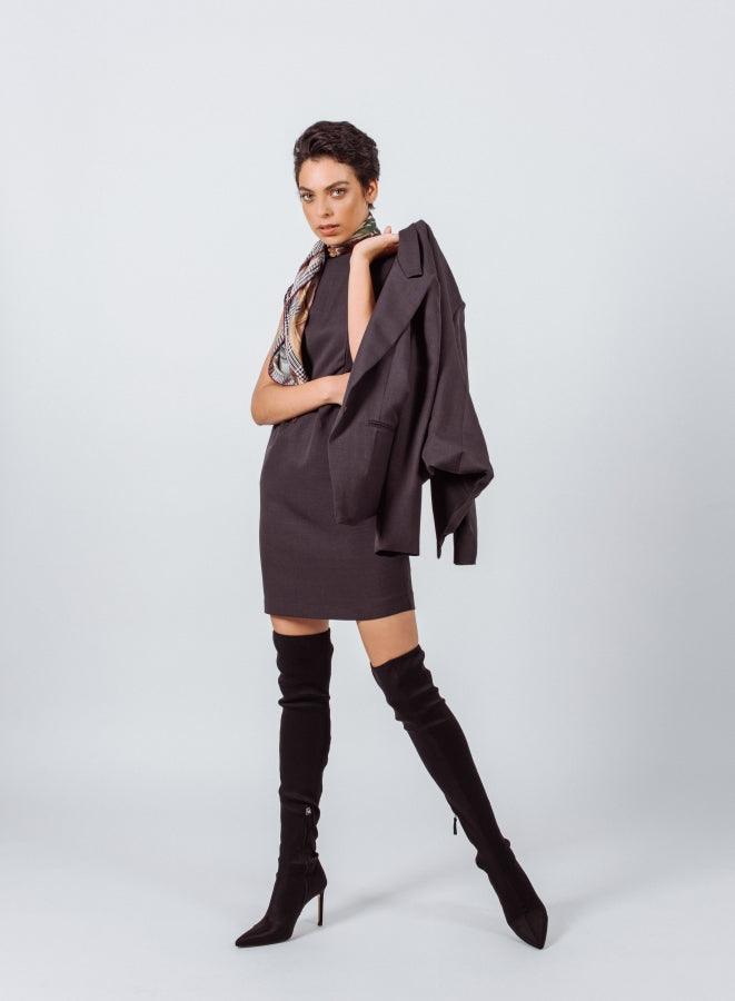 Woman wearing a brown dress and black knee-high boots on a white background
