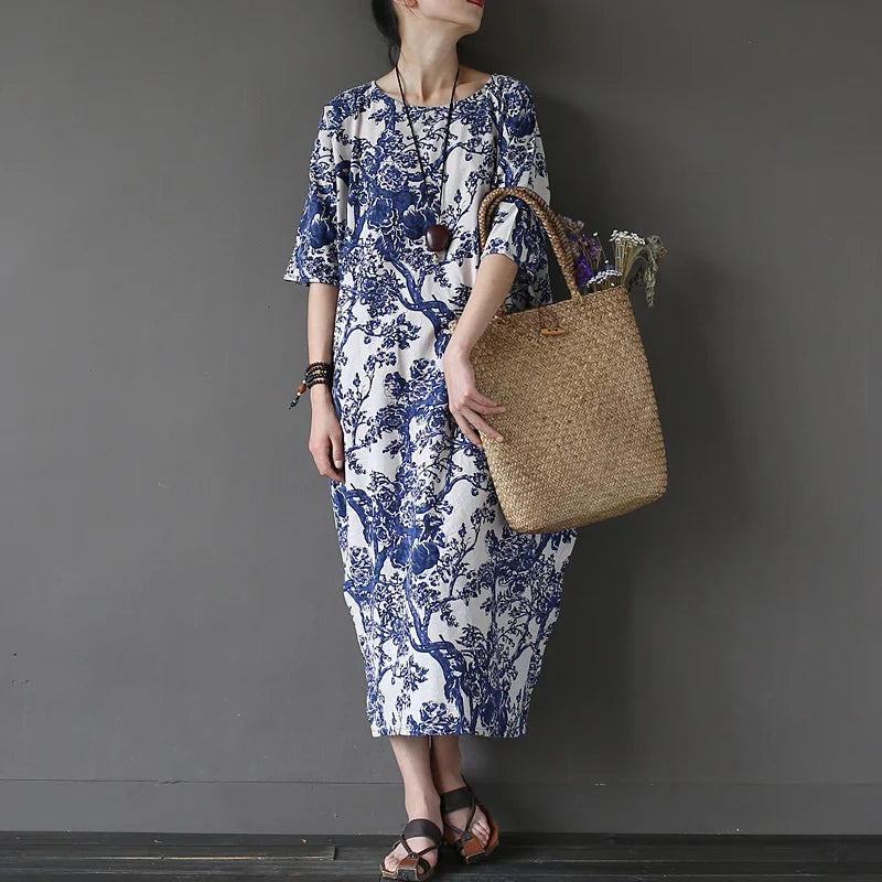 Woman wearing a blue and white floral dress holding a woven bag against a gray background