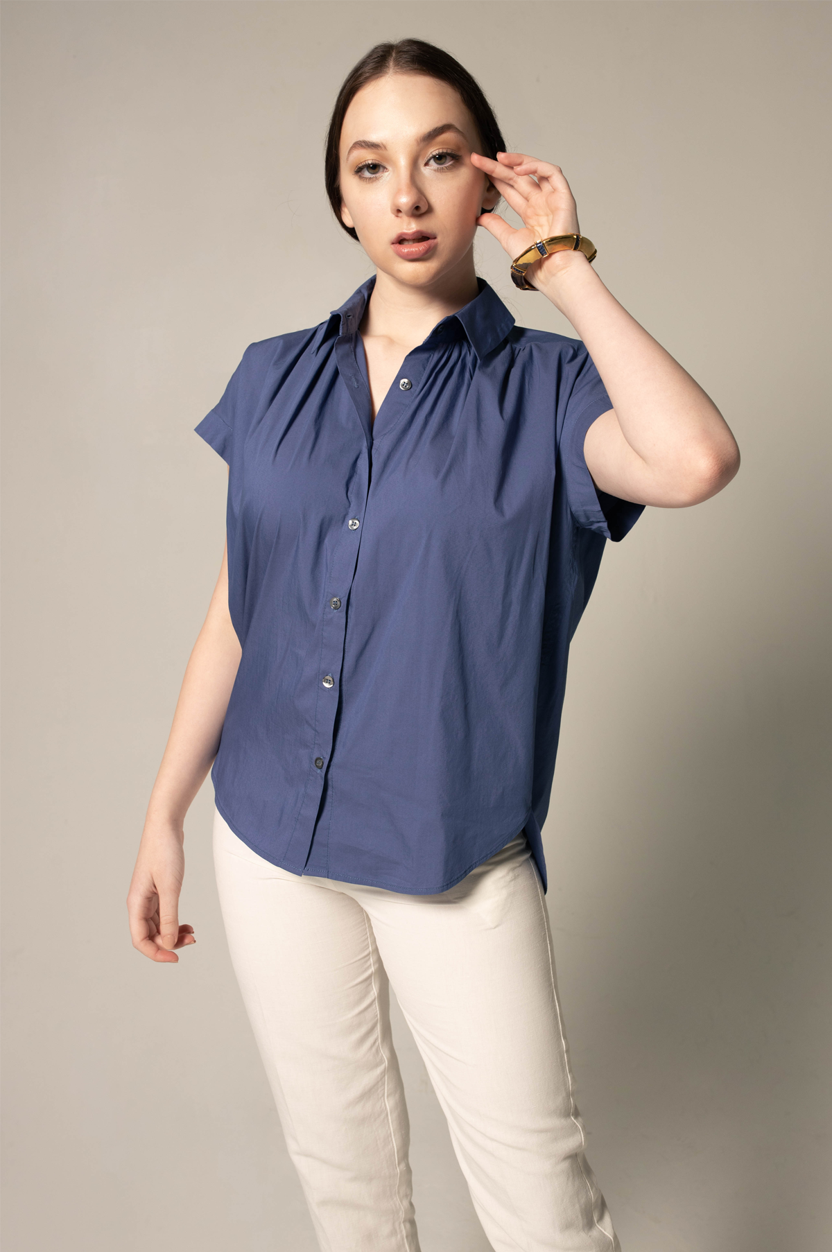 Woman wearing a blue sleeveless blouse and white pants against a beige background