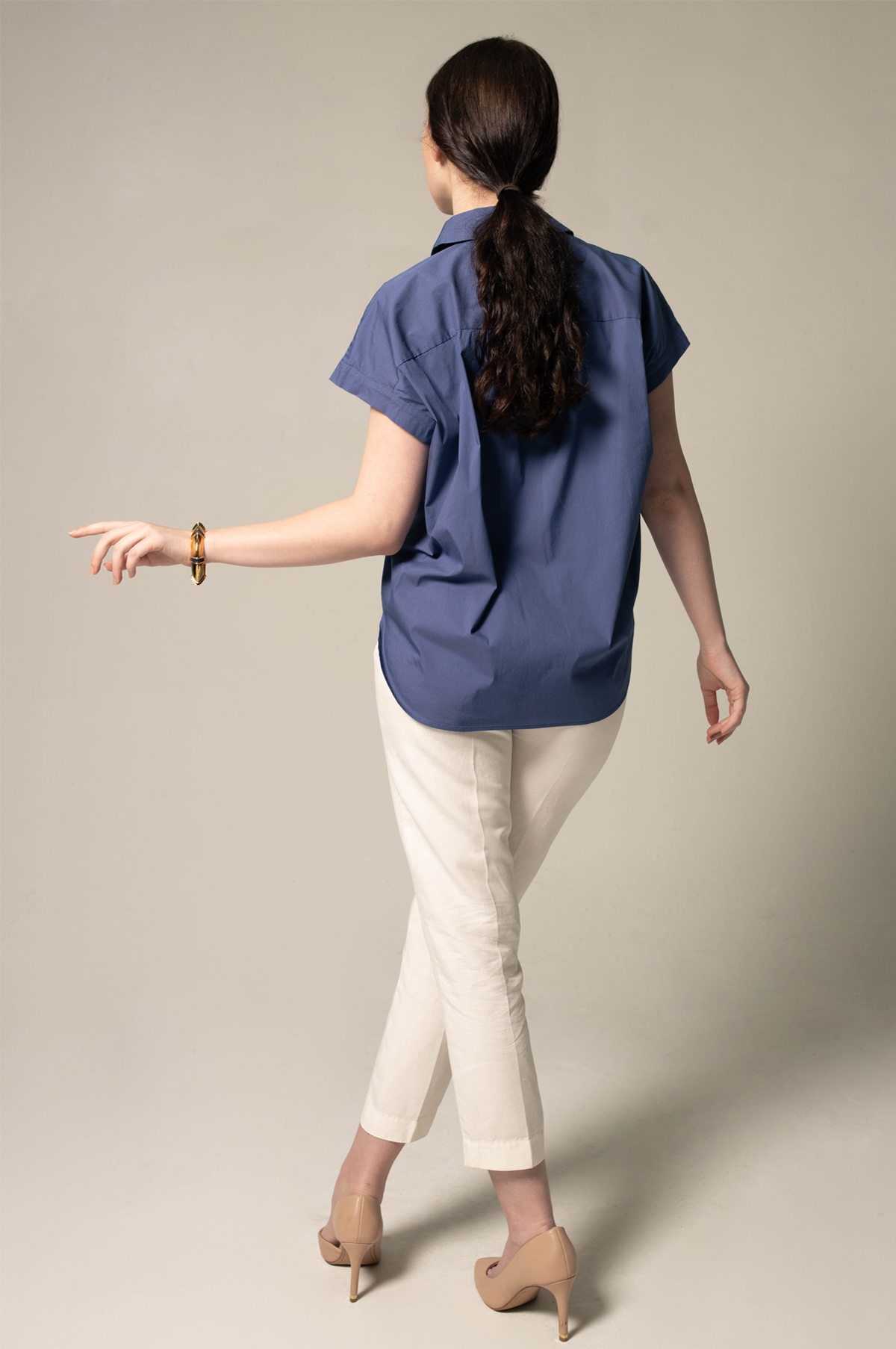 Woman wearing a blue shirt and white pants against a plain background