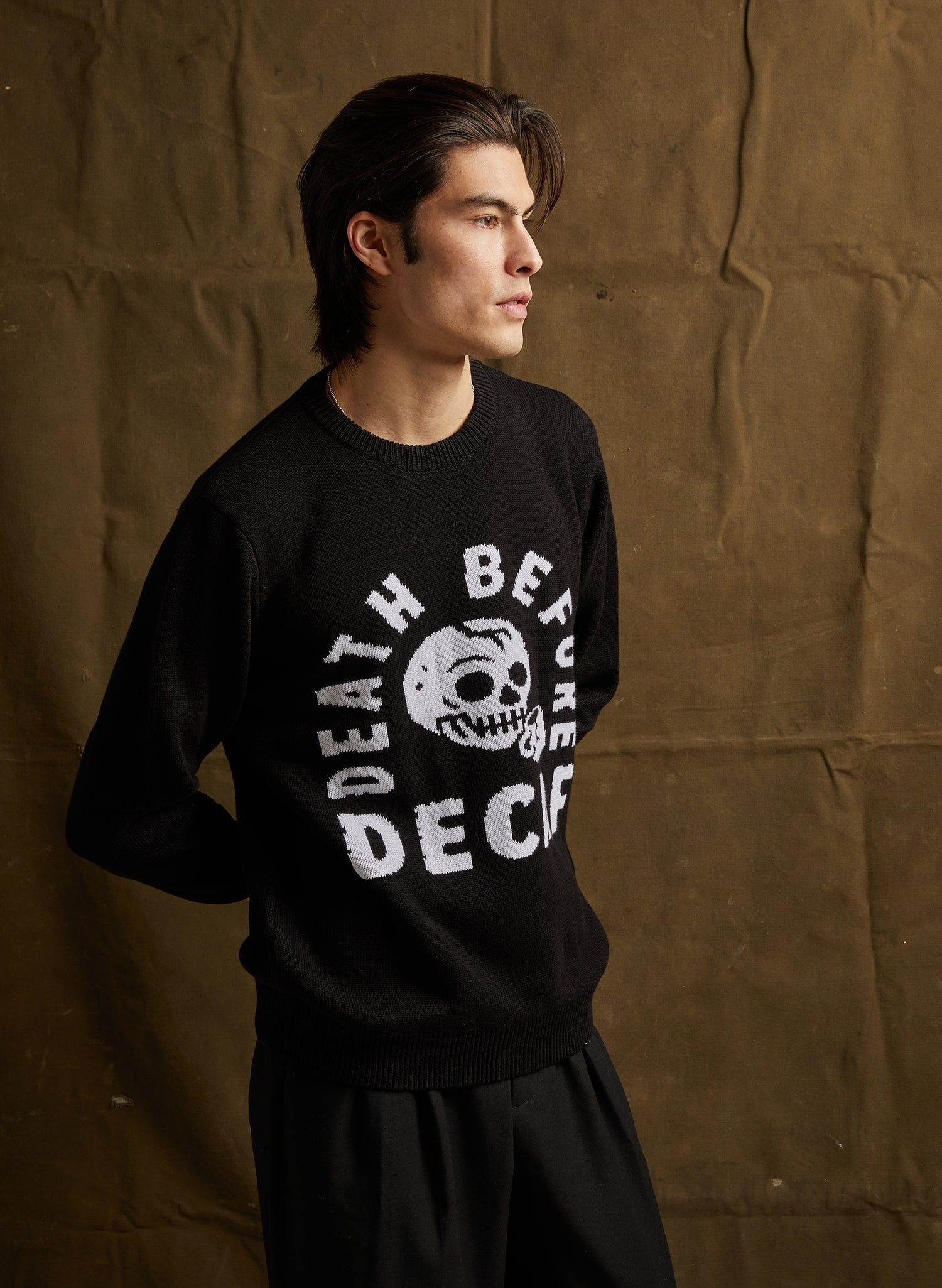 Person wearing a black sweatshirt with white text and graphic design against a brown textured background