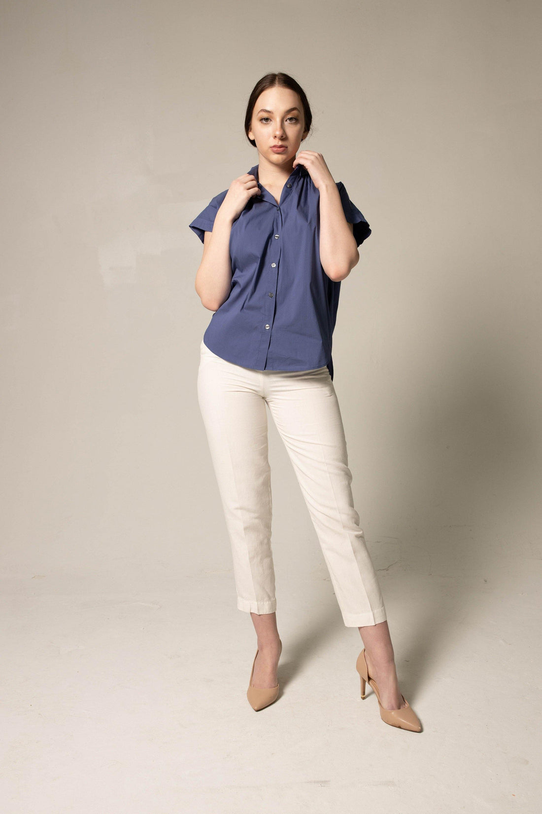 Woman wearing a blue shirt and white pants against a plain background