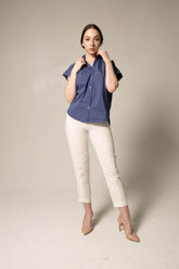 Woman wearing a blue shirt and white pants against a plain background