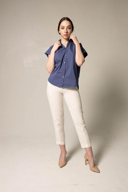 Woman wearing a blue shirt and white pants against a plain background