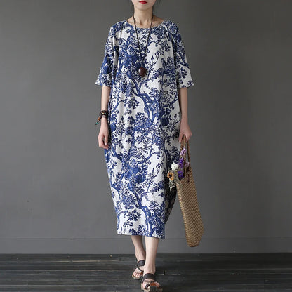 Woman wearing a blue and white floral dress holding a straw bag against a gray background