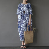 Person wearing a blue and white floral dress holding a woven bag against a gray background