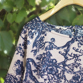 Blue and white floral patterned fabric on a wooden hanger against a green leafy background