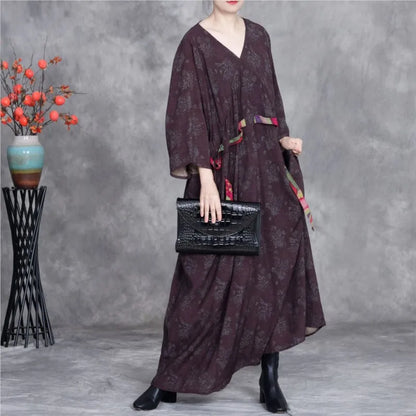 Person wearing a dark patterned dress holding a black handbag against a gray background