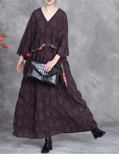Woman wearing a long dark dress holding a black handbag against a gray background
