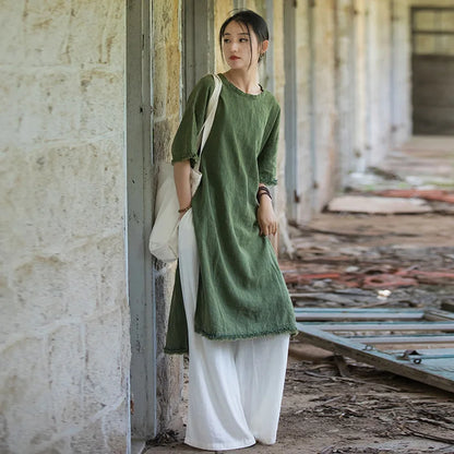 Woman in a green dress and white pants standing in an industrial setting.