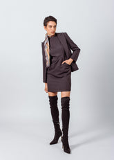 Woman wearing a brown dress with a matching blazer and black knee-high boots on a white background