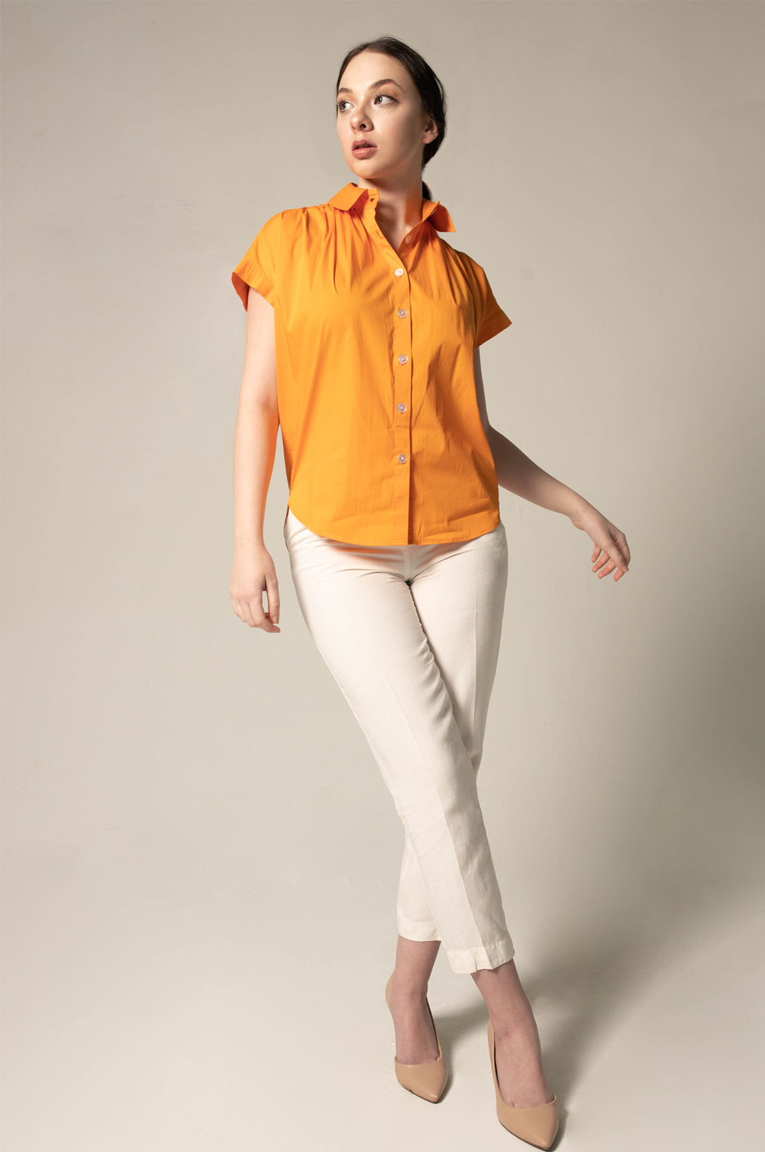 Woman wearing an orange blouse and white pants against a plain background