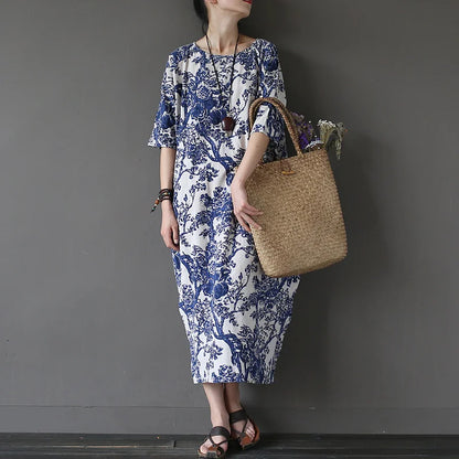 Woman wearing a blue and white floral dress holding a woven bag against a gray background