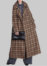 Person wearing a long plaid coat holding a black handbag against a gray background