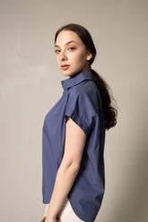 Woman wearing a blue sleeveless blouse against a beige background