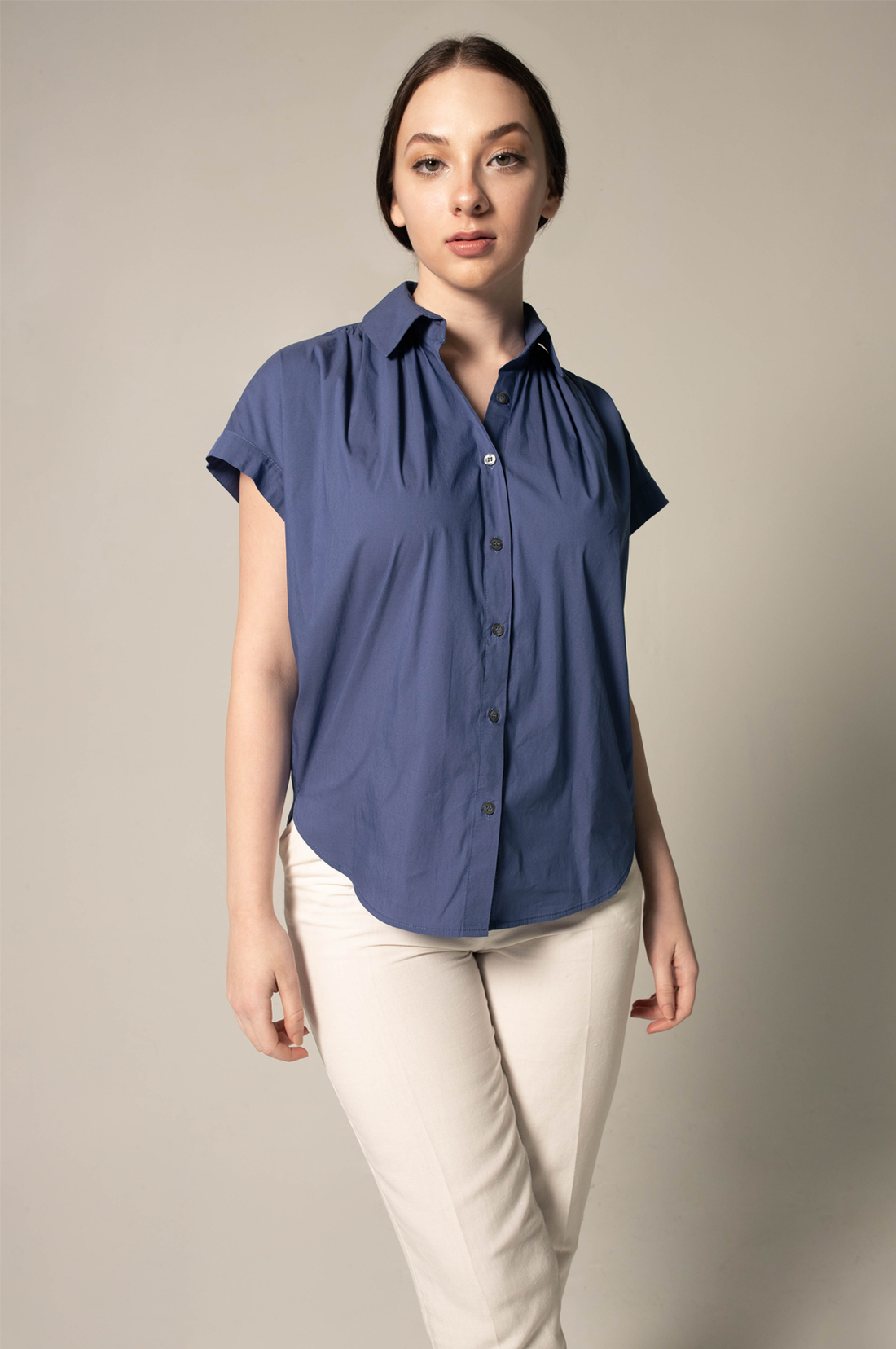 Woman wearing a blue shirt and white pants against a beige background