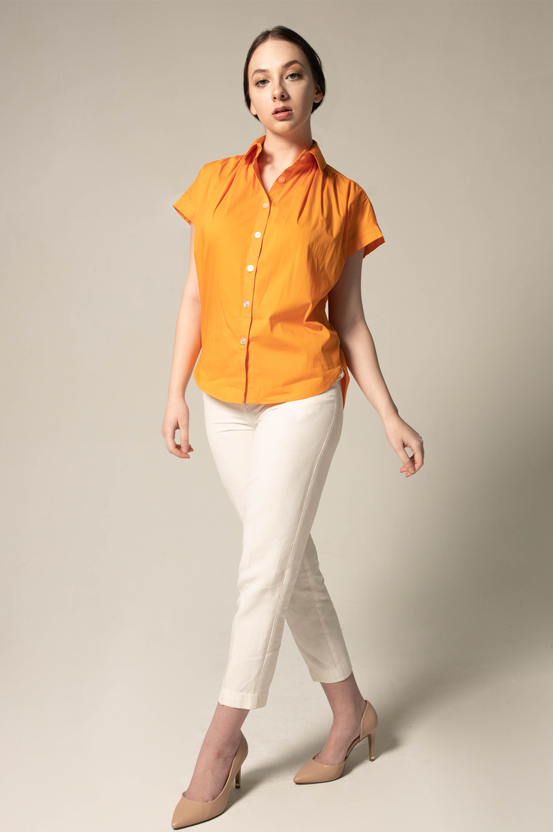 Woman wearing an orange shirt and white pants against a neutral background